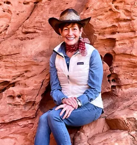 Woman in a cowboy hat sitting on red rock formations, smiling.