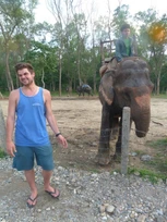 A man posing next to an elephant in a natural setting.