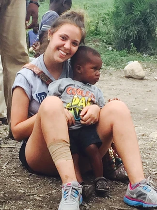 A young woman sits outdoors holding a small child on her lap.