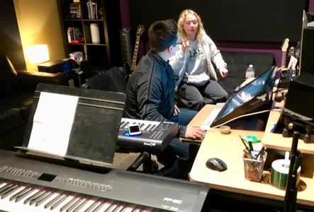 Two people collaborating in a music studio with keyboards and equipment.