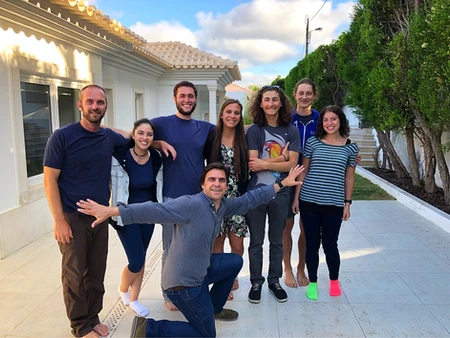 A group of eight friends posing happily outdoors in casual attire.