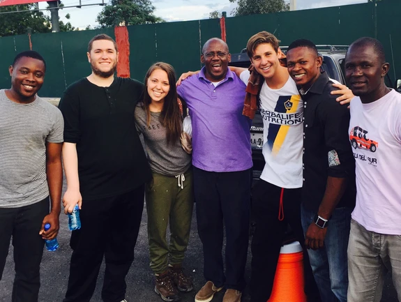 A group of five people smiling outdoors near a fence.