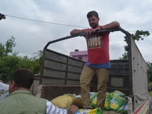 A man stands on a truck loaded with bags, talking to a seated person.