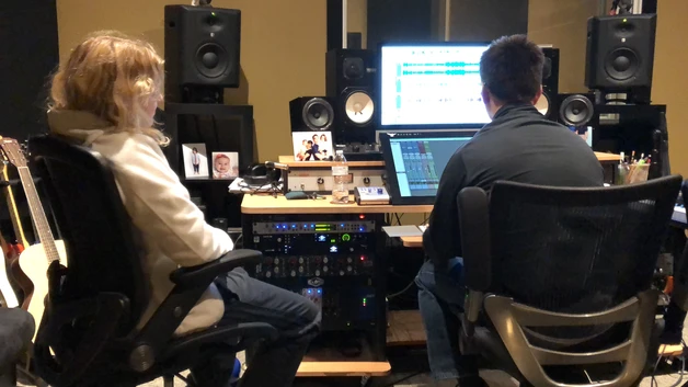 Two individuals working in a professional music recording studio.