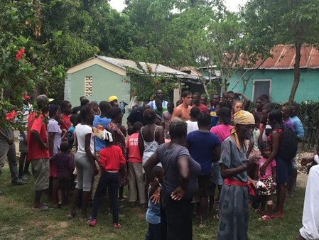 A large group of people gathered outdoors near houses in a rural setting.