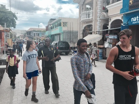 A group of young people walking on a street with buildings and cars.