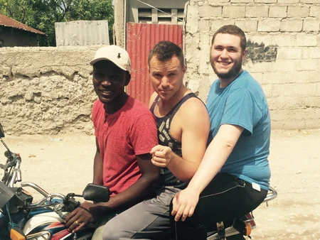 Three men sitting closely on a motorcycle outdoors.
