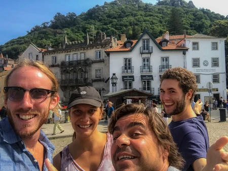 Four friends smiling in front of a historic building with greenery in the background.