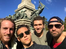 Four friends taking a selfie in front of a historic monument on a sunny day.