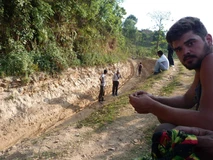 People standing along a dug trench in a rural area.