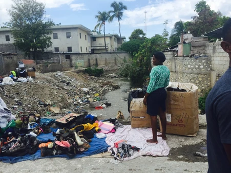 People sorting clothes on a street near a drainage area.