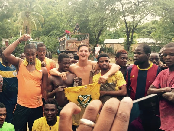 A group of young men posing outdoors with a smiling woman in the center.
