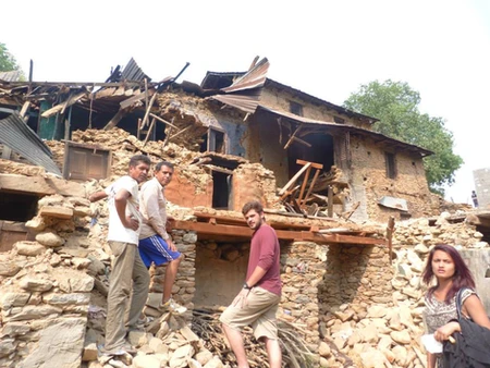 Two men carrying wooden planks near a damaged brick house.
