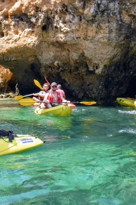 People kayaking near a rocky cave in clear water.