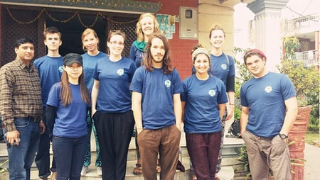 Group of young adults in blue shirts posing on steps outdoors.