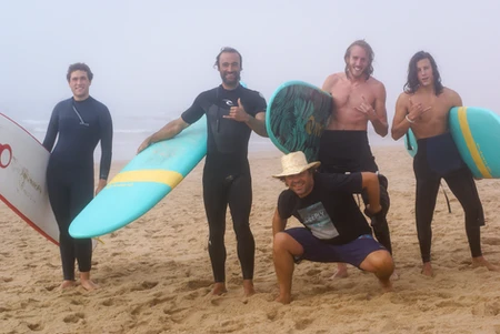 Group of surfers posing on the beach with surfboards.
