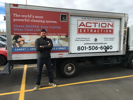 Man standing confidently beside an Action Extraction truck with company details.