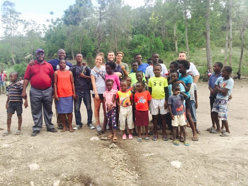 A diverse group of adults and children posing outdoors in a natural setting.