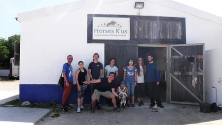 Group of people and a dog outside a stable named Horses R Us.