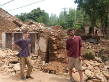 Two young men stand in front of a collapsed stone structure outdoors.