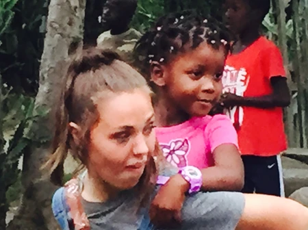 A woman carrying a young girl on her back outdoors.