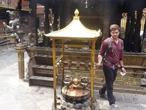 A man stands beside a traditional incense burner with a golden roof in a temple.