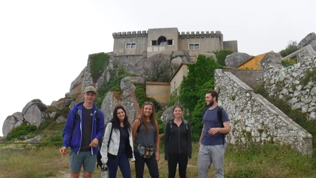 Five people posing in front of a stone castle on a hill.