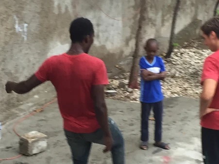 Two boys playing soccer near a wall.
