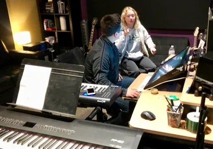Two people collaborating in a music studio with keyboards and equipment.