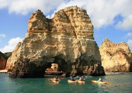 Kayakers paddling near large coastal cliffs with caves under a blue sky.