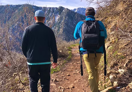 Two hikers walking on a rocky mountain trail surrounded by nature.