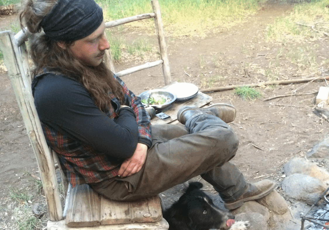 Man sitting on a rustic chair with a dog resting at his feet outdoors.