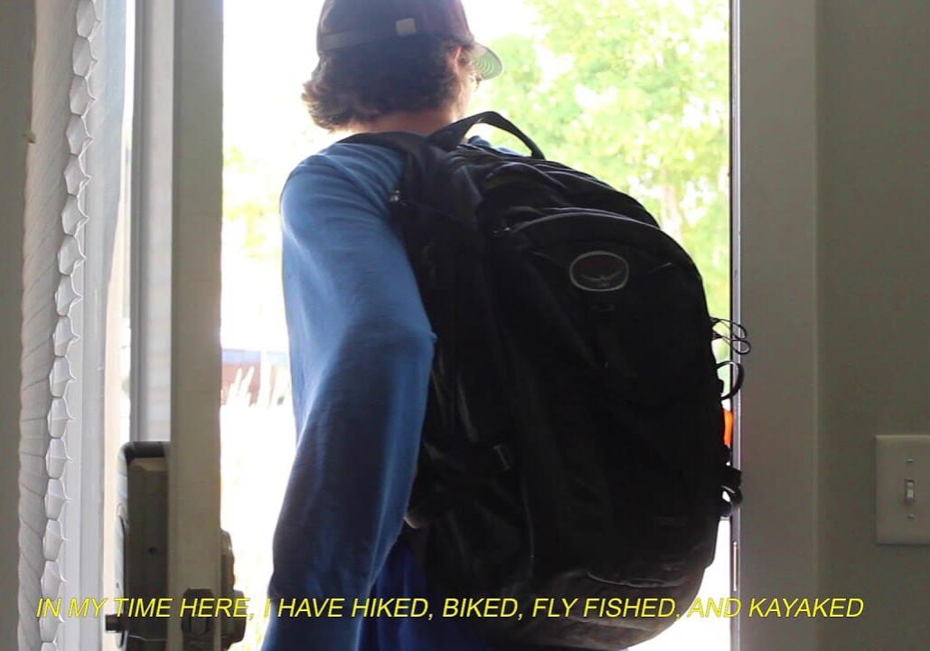 Person with a backpack looking out of a door into a bright outdoor area.