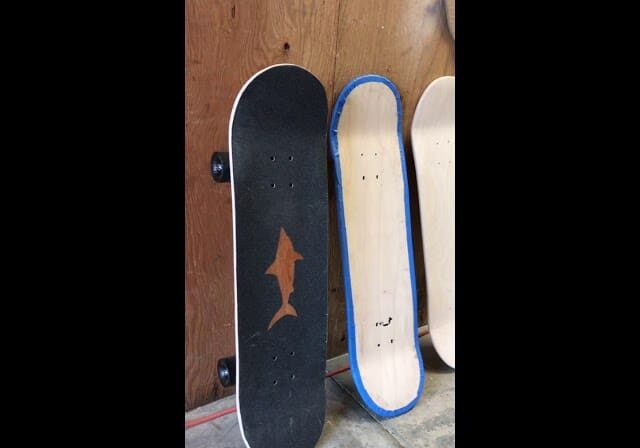 Three skateboards leaning against a wooden wall, one with a shark graphic.